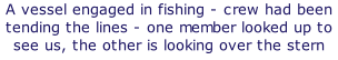 A vessel engaged in fishing - crew had been tending the lines - one member looked up to see us, the other is looking over the stern