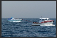 A small motor boat towing a dismasted yacht