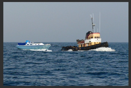 A dismasted yacht being towed by a harbour or coastal tug