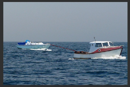 A dismasted yacht being towed by a small motor boat